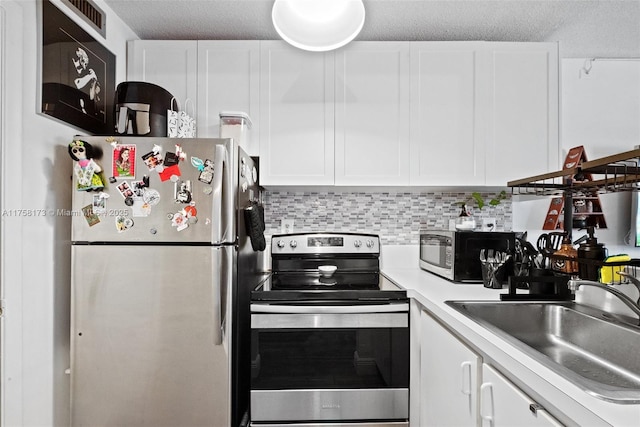 kitchen featuring stainless steel appliances, a sink, white cabinets, light countertops, and decorative backsplash