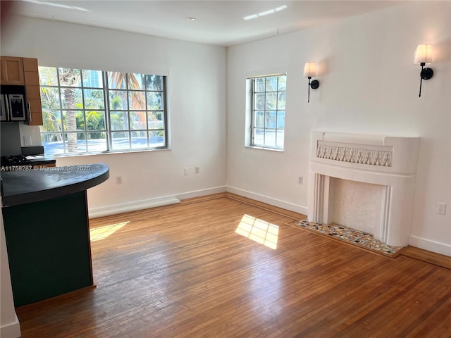 unfurnished living room featuring light wood-style flooring, baseboards, a wealth of natural light, and a fireplace with flush hearth