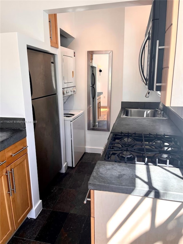 kitchen with dark countertops, freestanding refrigerator, stacked washing maching and dryer, black microwave, and baseboards