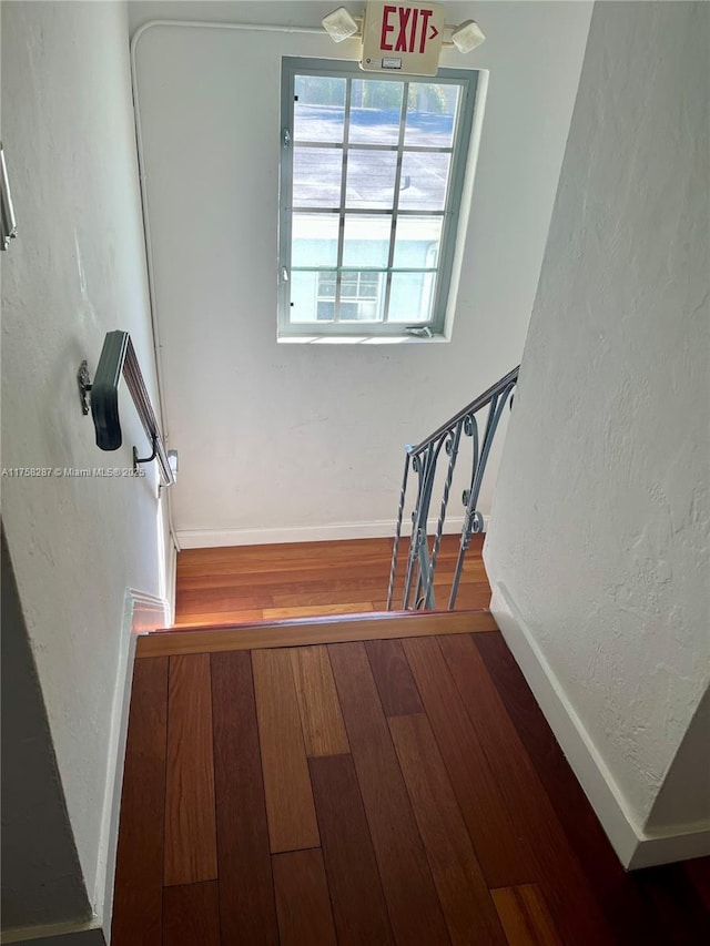 stairs featuring a textured wall, hardwood / wood-style flooring, and baseboards