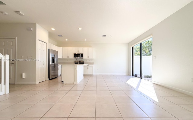 kitchen featuring light tile patterned flooring, open floor plan, light countertops, appliances with stainless steel finishes, and a center island with sink