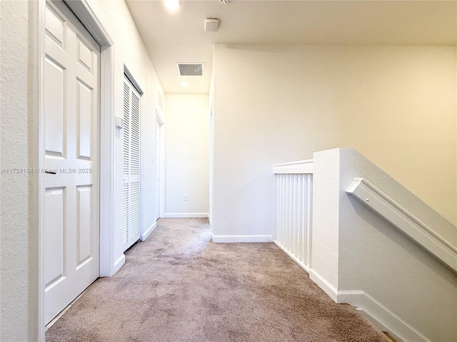 corridor with carpet, baseboards, visible vents, and an upstairs landing