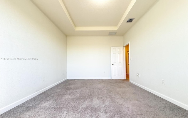 unfurnished room with a tray ceiling, carpet, visible vents, and baseboards