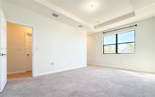 carpeted spare room featuring a raised ceiling, visible vents, and baseboards