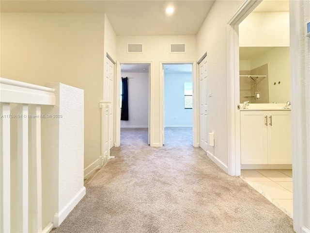 corridor featuring light colored carpet, visible vents, and baseboards