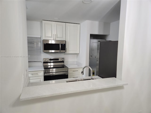 kitchen with stainless steel appliances, white cabinetry, a sink, and light stone countertops