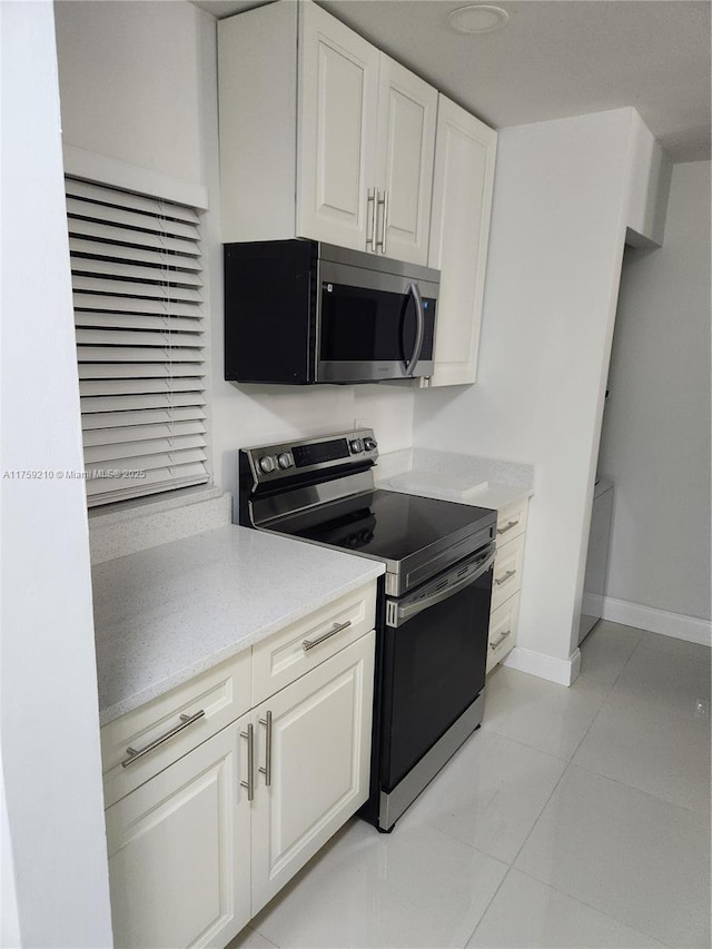 kitchen featuring light tile patterned floors, light stone counters, white cabinetry, baseboards, and appliances with stainless steel finishes