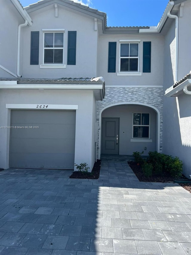 view of front of house with decorative driveway, a tile roof, stucco siding, an attached garage, and stone siding