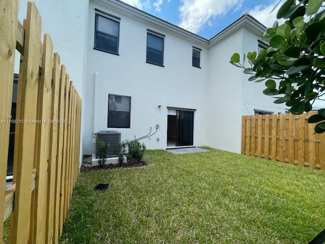 rear view of house with stucco siding, fence, a lawn, and central AC unit