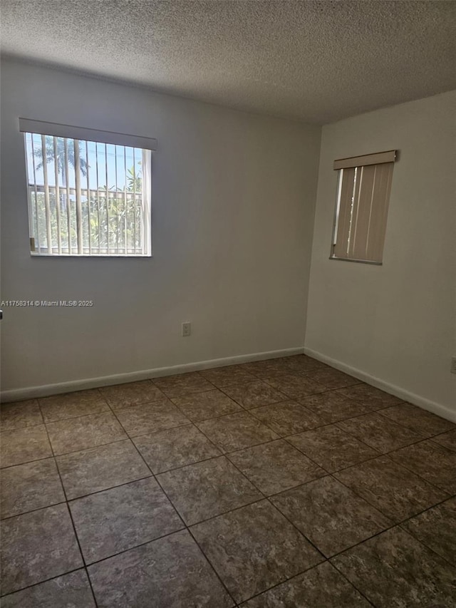 empty room with dark tile patterned floors, baseboards, and a textured ceiling