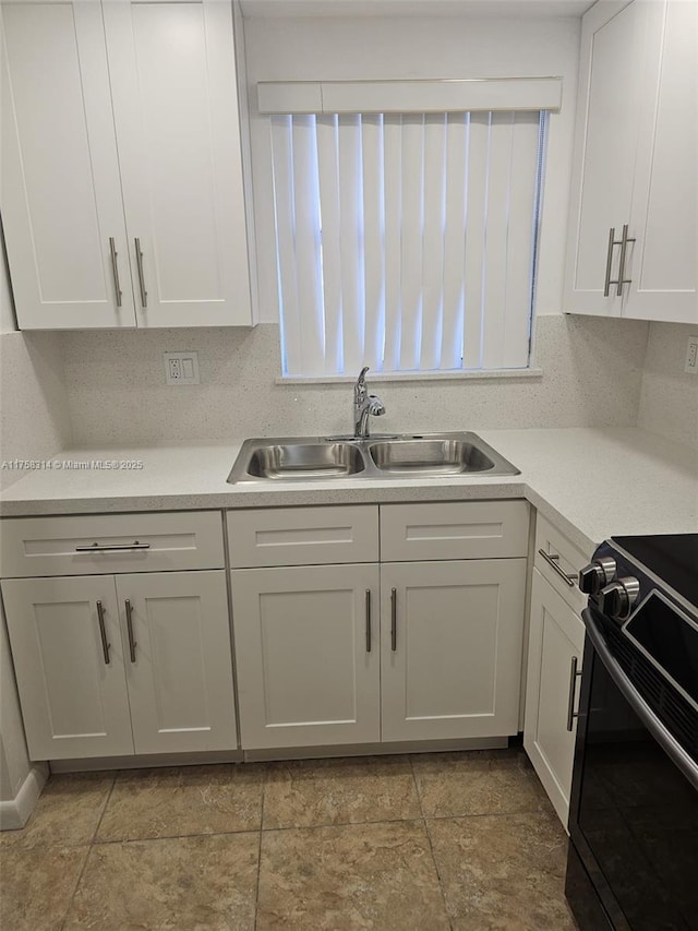 kitchen featuring light countertops, black range with electric stovetop, decorative backsplash, white cabinets, and a sink