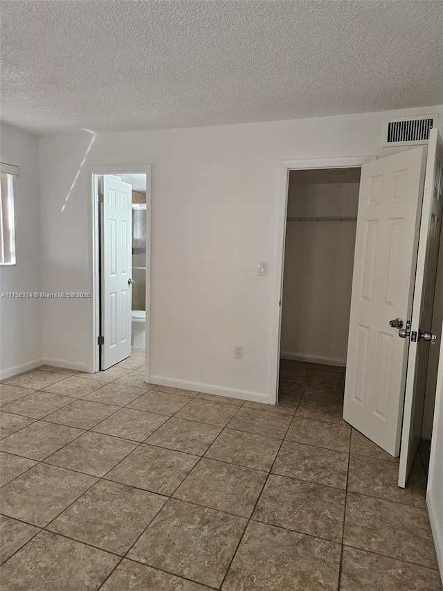 unfurnished bedroom featuring a textured ceiling, a spacious closet, visible vents, and a closet