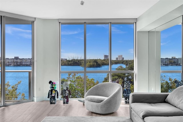 living area with floor to ceiling windows, wood finished floors, and a water view