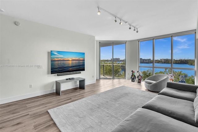 living area featuring track lighting, floor to ceiling windows, wood finished floors, and baseboards