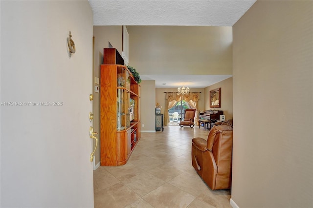 hallway featuring light tile patterned floors, baseboards, a towering ceiling, a textured ceiling, and a notable chandelier