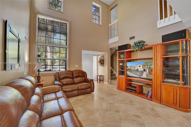 living room featuring light tile patterned floors, visible vents, stairway, a high ceiling, and baseboards