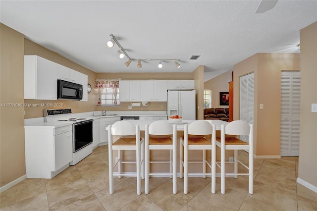 kitchen with light countertops, a breakfast bar, white appliances, and visible vents