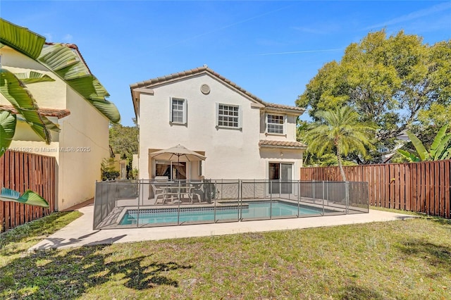 back of property with a fenced in pool, a tile roof, stucco siding, a lawn, and a fenced backyard