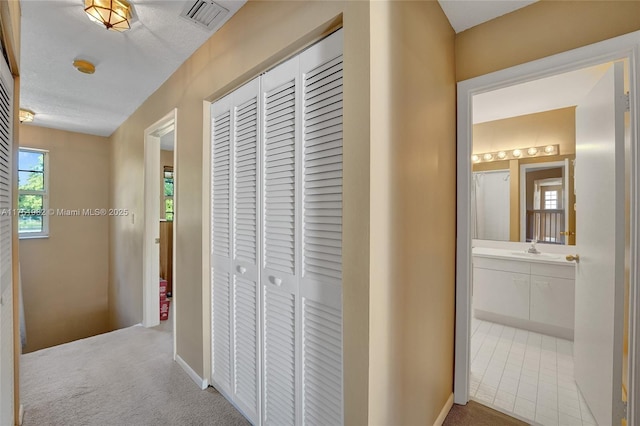 corridor with carpet floors, visible vents, and a sink