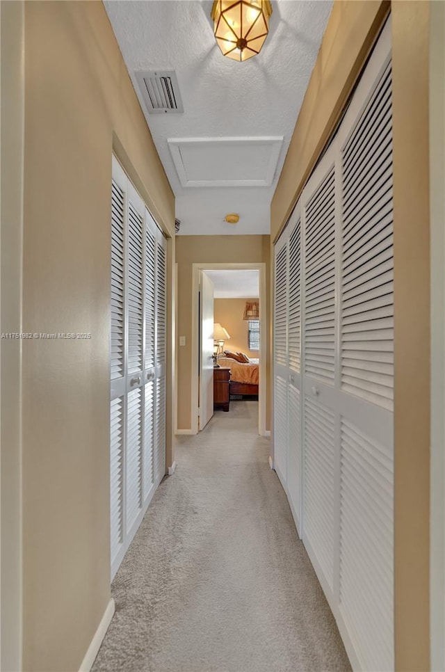 hallway with attic access, visible vents, light carpet, and baseboards