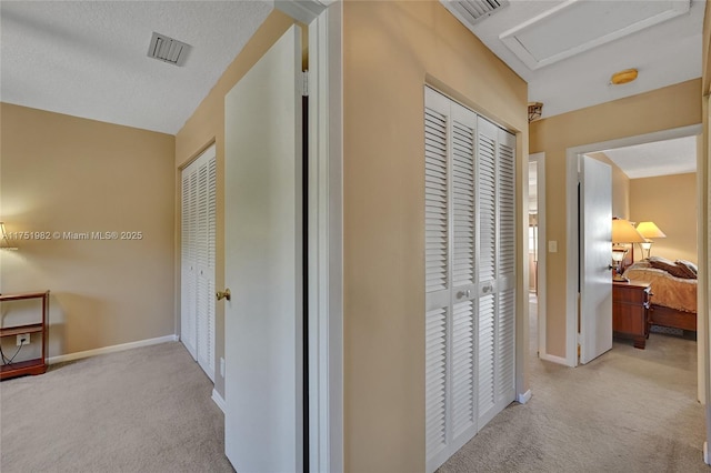 hall with attic access, carpet flooring, visible vents, and baseboards