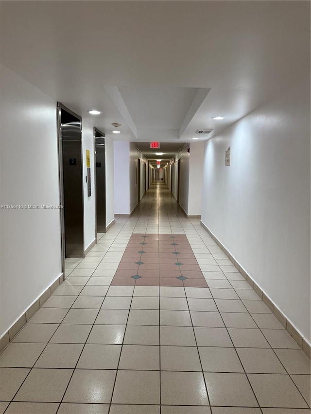 hall with elevator, baseboards, and light tile patterned flooring