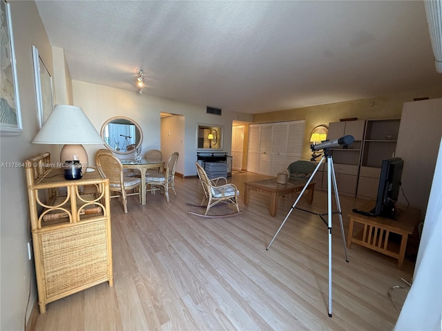 living area with baseboards, a textured ceiling, visible vents, and wood finished floors