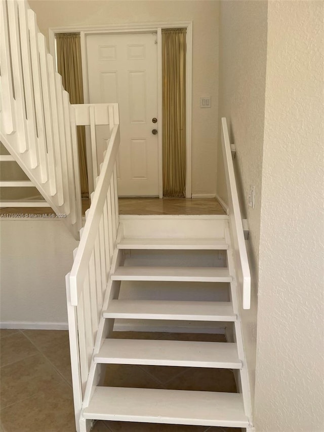 stairs featuring tile patterned flooring, baseboards, and a textured wall