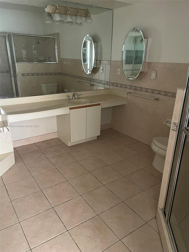 bathroom featuring toilet, tile patterned flooring, an enclosed shower, and tile walls