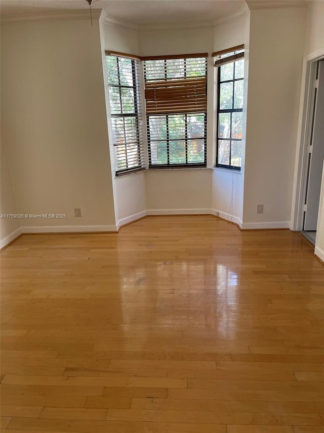 empty room with crown molding, baseboards, a wealth of natural light, and light wood-style floors