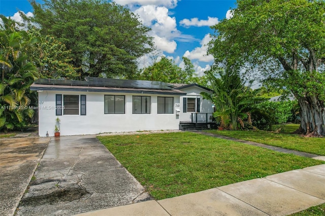 view of front of property with stucco siding, a front lawn, and solar panels