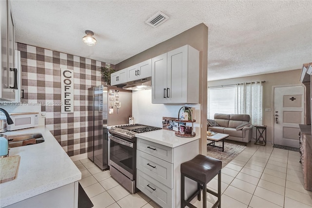 kitchen featuring visible vents, white microwave, open floor plan, under cabinet range hood, and stainless steel range with gas cooktop