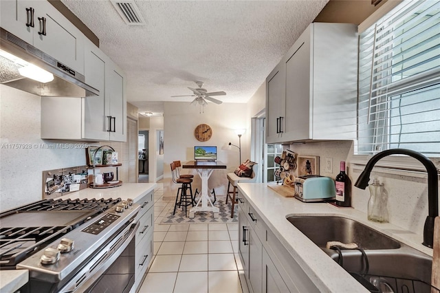 kitchen with light tile patterned flooring, under cabinet range hood, a sink, visible vents, and stainless steel range with gas stovetop