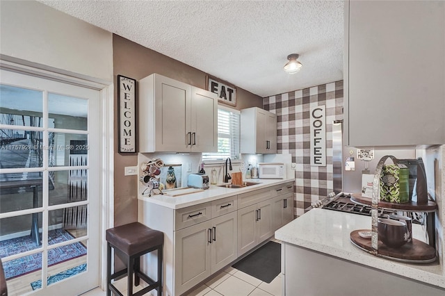 kitchen with white microwave, light tile patterned flooring, a sink, a textured ceiling, and wallpapered walls