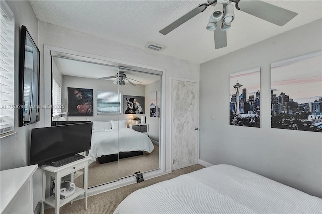 bedroom with a textured ceiling, ceiling fan, carpet flooring, and visible vents