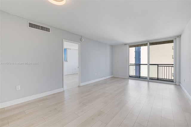 spare room featuring a wall of windows, light wood-type flooring, visible vents, and baseboards