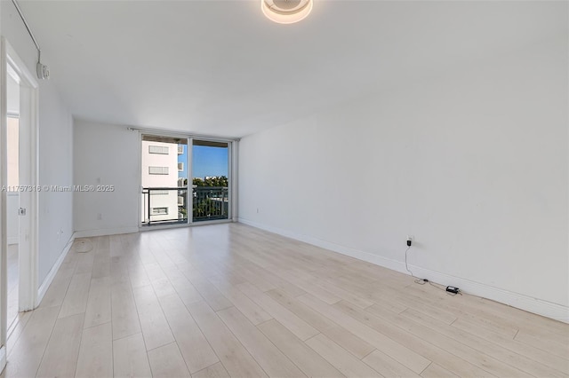 unfurnished room featuring expansive windows, baseboards, and light wood finished floors