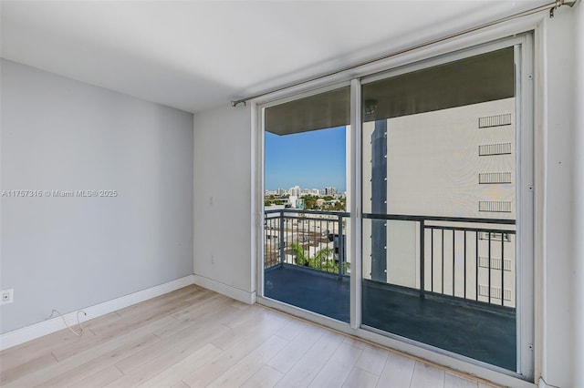 unfurnished room featuring floor to ceiling windows, baseboards, a city view, and wood finished floors