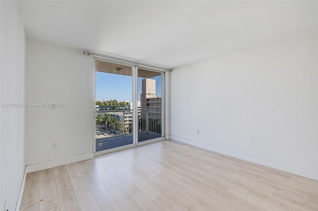 empty room featuring a wall of windows, wood finished floors, and baseboards