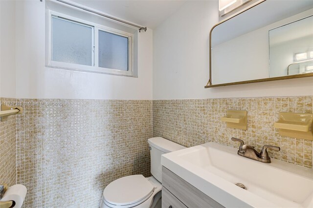 half bathroom with toilet, a wainscoted wall, tile walls, and a sink