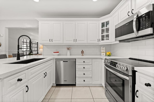 kitchen with decorative backsplash, stainless steel appliances, white cabinetry, a sink, and light tile patterned flooring