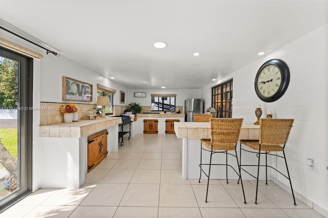 kitchen featuring a peninsula, a wealth of natural light, light tile patterned flooring, and freestanding refrigerator