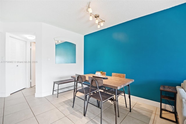 dining area with a textured ceiling, light tile patterned floors, rail lighting, and baseboards