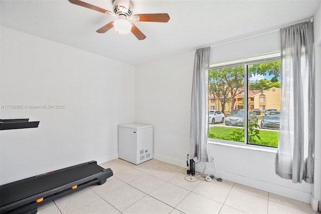 exercise room featuring light tile patterned floors, ceiling fan, and baseboards