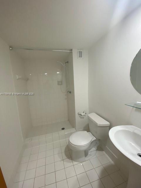 bathroom with visible vents, toilet, tile patterned floors, a tile shower, and a sink