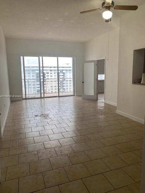 tiled empty room with high vaulted ceiling, a ceiling fan, and baseboards