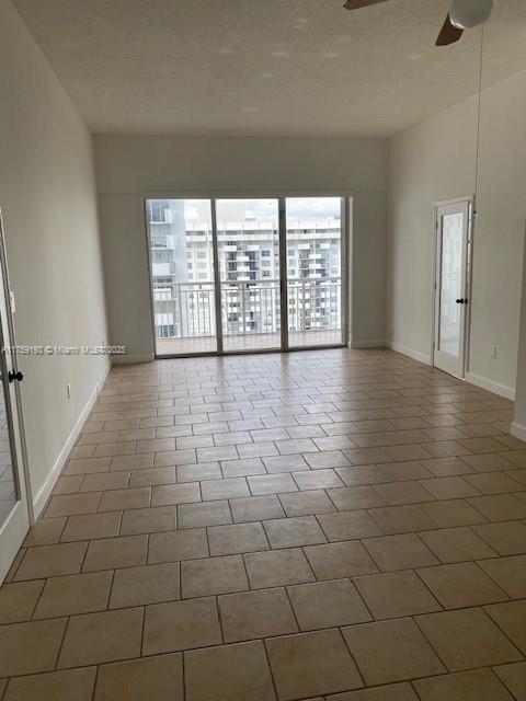 unfurnished room featuring a ceiling fan, tile patterned flooring, a textured ceiling, and baseboards