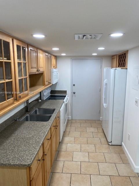 kitchen featuring white appliances, baseboards, visible vents, dark stone counters, and a sink