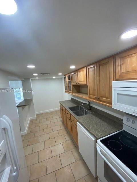 kitchen featuring dark countertops, white appliances, a sink, and recessed lighting