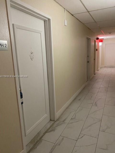 hall with marble finish floor, a paneled ceiling, and baseboards